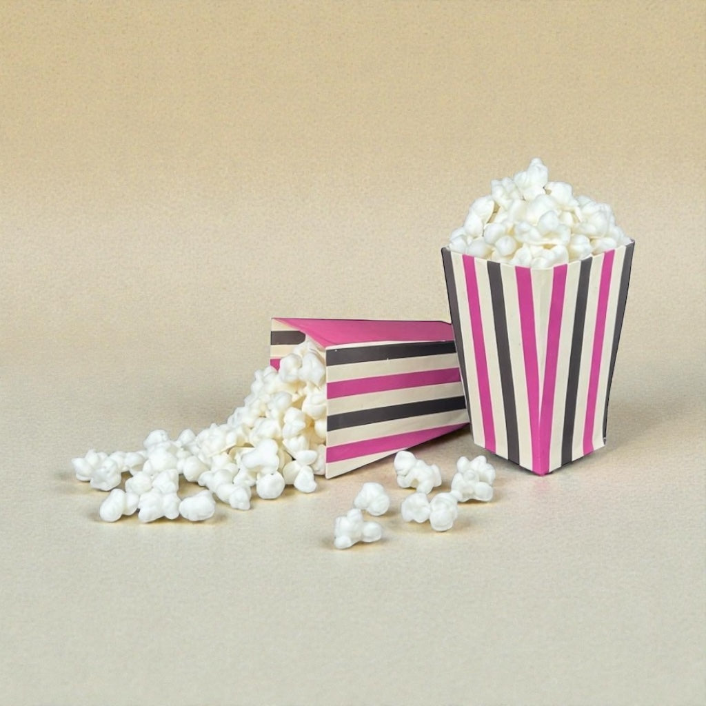 Two striped popcorn buckets with popcorn wax melts spilling out on a beige background